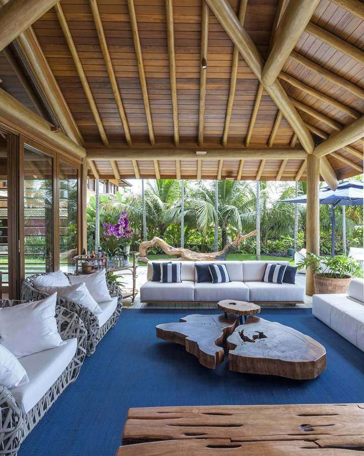Lounge coberto com sofás brancos, tapete azul e mesas de tronco