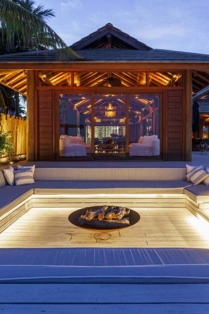Lounge externo com fogueira e bancos almofadados, ao anoitecer