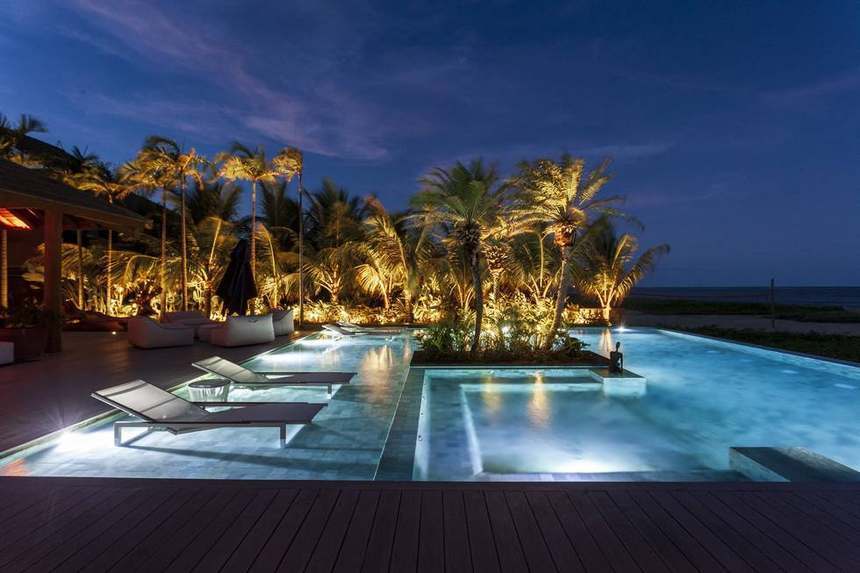 Piscina iluminada à noite, com o mar ao fundo
