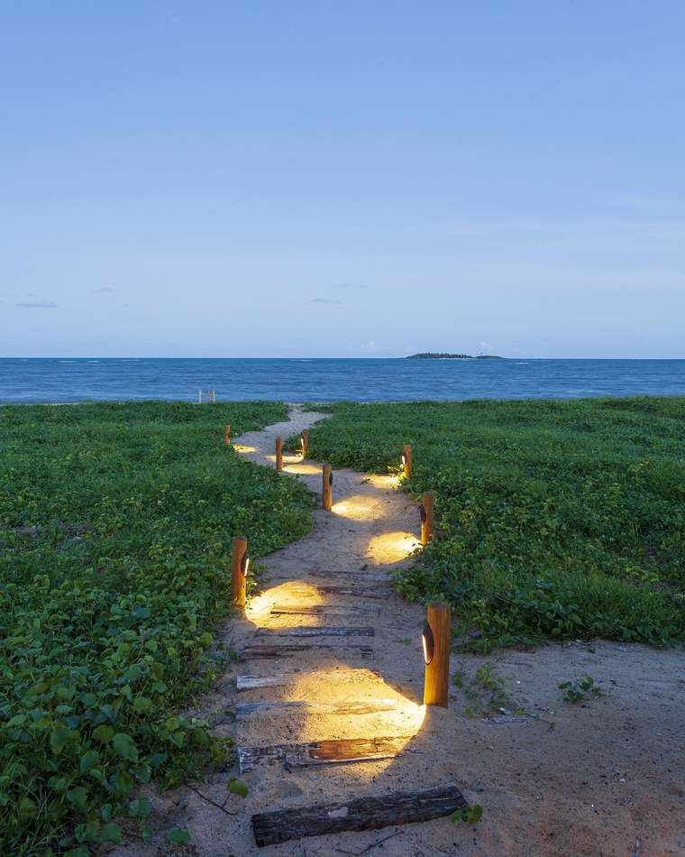 Caminho de areia iluminado até a praia, com a Ilha de Santo Aleixo no horizonte